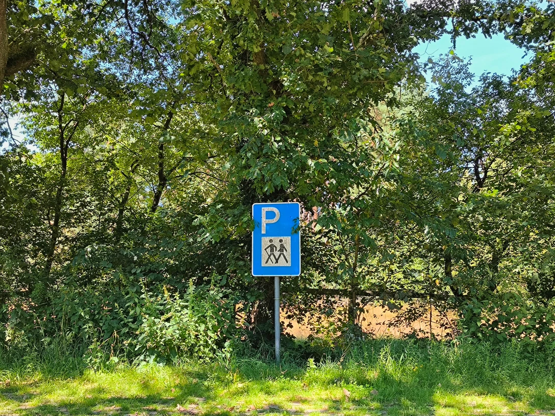 Wanderparkplatz Ems-Infozentrum Parkplatzschild für Wanderer umgeben von grünen Bäumen, ein sonniger Tag in einer Waldlichtung.