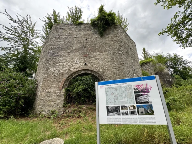 Kalköfen Ruine eines alten, von der Natur überwucherten Steinbaus mit Informationstafel im Vordergrund.