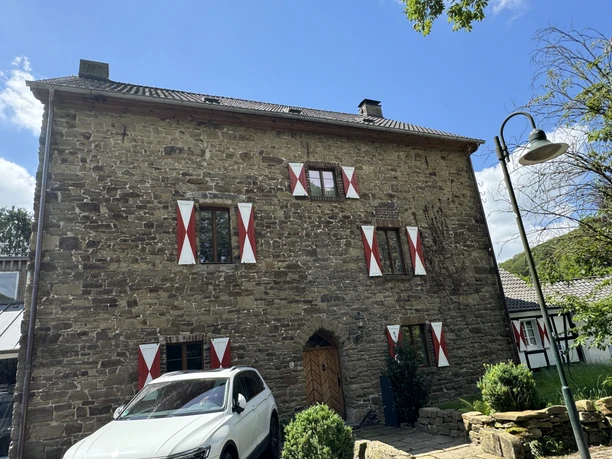 Burghaus Scheltensülz Außenansicht Ein rustikales Steingebäude mit rot-weißen Fensterläden, davor ein weißes Auto geparkt.