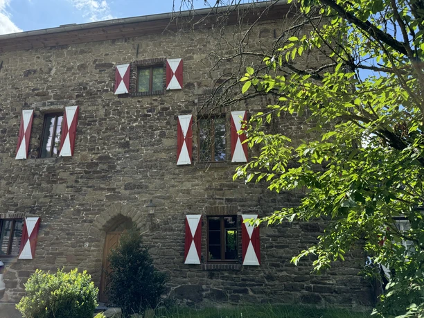 Burghaus Scheltensülz Altes steinernes Haus mit weißen Fensterläden, umgeben von grünem Laub und Natur.