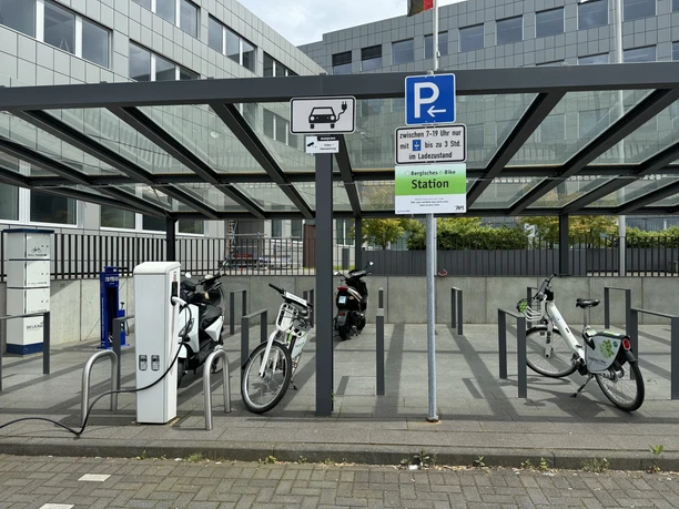 Kreishaus Heidkamp (Ladesäule) Barrierefreie Ladestation für Elektrofahrzeuge und Fahrräder mit überdachtem Bereich in städtischer Umgebung.