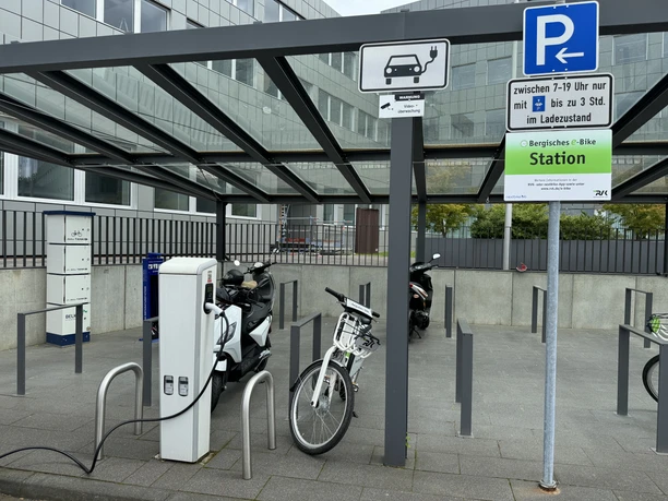 Ladesäule Barrierefreie E-Bike-Ladestation mit überdachten Abstellplätzen vor einem modernen Gebäude.