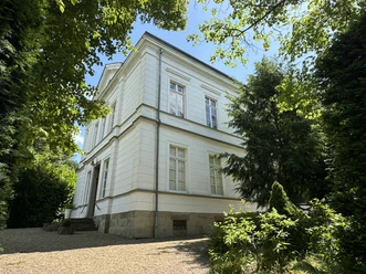 Villa Longrée - Straßenansicht Historische weiße Villa mit erhabener Fassade, umgeben von üppigem, grünem Garten unter blauem Himmel.