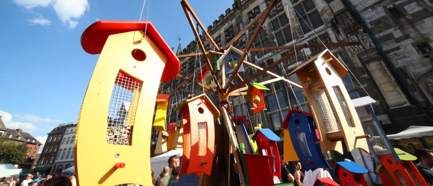 Vor dem Aachener Rathaus steht ein Stand mit bunt angemalten Vogelhäusern aus Holz.