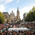 Eine vollbesetzte Zuschauertribüne umrahmt das Spektakel des Stabhochsprungs vor der Aachener Kathedrale.