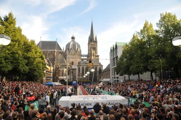 NetAachen Domspringen Eine vollbesetzte Zuschauertribüne umrahmt das Spektakel des Stabhochsprungs vor der Aachener Kathedrale.
