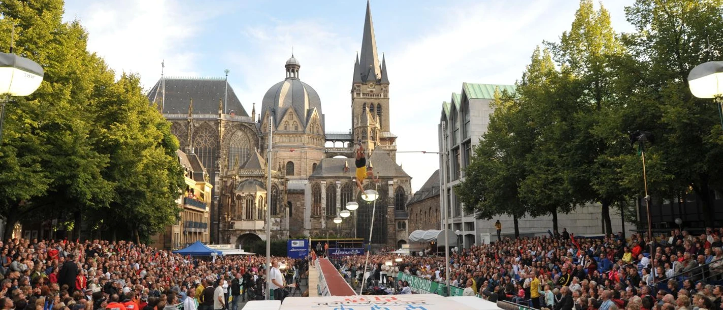 NetAachen Domspringen Eine vollbesetzte Zuschauertribüne umrahmt das Spektakel des Stabhochsprungs vor der Aachener Kathedrale.