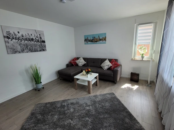 Ferienwohnung Haufe, Wohnraum Heller Wohnraum mit grauem Sofa, Couchtisch, Wandbildern, einem Teppich und hellem Holzfußboden.