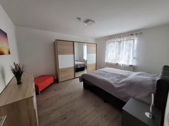 Ferienwohnung Haufe, Schlafraum Moderner Schlafraum mit Doppelbett, großem Schrank, Nachttisch und rotem Sitzhocker, hell dekoriert.