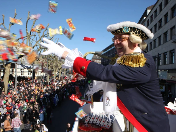 Rosenmontagszug Aachen Ein verkleideter Karnevalsprinz wirft Süßigkeiten von seinem Umzugswagen in die Menge. Viele fröhliche Menschen stehen an den Straßenrändern und schauen begeistert dem bunten Treiben zu.
