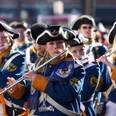 Musikerinnen in blauen Uniformen und historischen Hüten spielen Flöte beim Rosenmontagszug in Aachen.