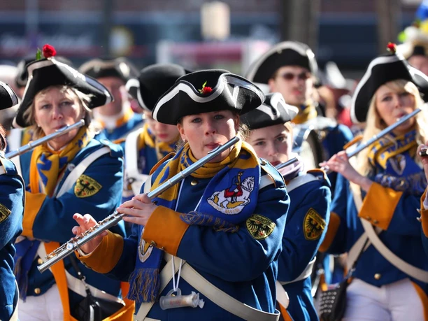 Musikerinnen in blauen Uniformen und historischen Hüten spielen Flöte beim Rosenmontagszug in Aachen.
