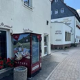 Proviantomat Standort am Hotel "Zur Post" Ein roter Verkaufsautomat steht vor einem Hotel mit der Aufschrift "Hotel Zur Post", daneben blühende rote Geranien.