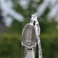 Trinkwasserspender_Greffen 009.jpg Ein silberner Trinkbrunnen sprudelt klares Wasser, umgeben von unscharfem Grün im Hintergrund.