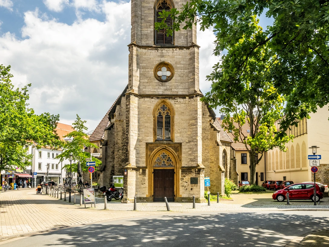 Süsterkirche Bielefeld Historische Kirche mit hohem Turm, umgeben von Bäumen und blauem Himmel in urbanem Umfeld.