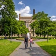 Ravensberger Park Bielefeld Ein Paar spaziert auf einem gepflasterten Weg durch eine grüne Allee vor einem historischen Gebäude.