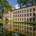 Ravensberger Spinnerei Bielefeld Ein historisches Backsteingebäude spiegelt sich malerisch in einem ruhigen Teich, umgeben von Grün.