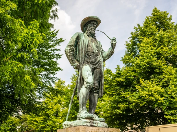 Leineweber-Denkmal Bielefeld Bronzestatue eines Mannes in traditioneller Tracht mit Pfeife, umgeben von grünen Bäumen.