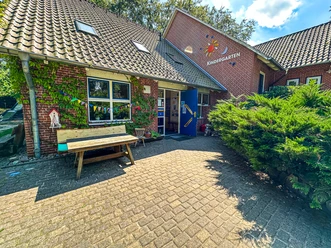 Kindergarten Oldendorf-Luhe (6).jpg Eingangsbereich des Kindergartens Oldendorf mit Backsteinfassade, Bank und buntem Wimpelschmuck.