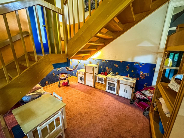 Spielecke mit Kinderküche und Puppenwagen unter einer Holztreppe im Kindergarten.