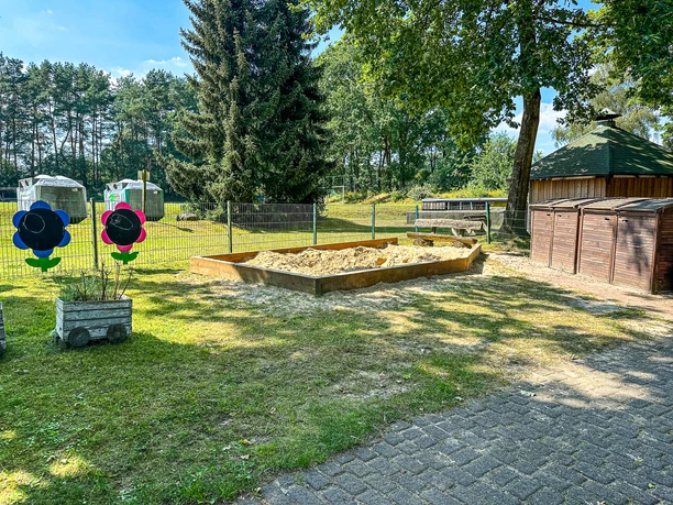Kindergarten Oldendorf-Luhe (24).jpg Sandkasten im Außenbereich des Kindergartens mit Blumen-Tafeln und Holzunterstand.