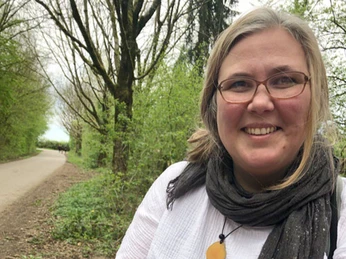 Naturerlebnisse mit Sandra Hoitz in der Wilden Werkstatt Sandra Hoitz lächelt in die Kamera, während sie in einer grünen, bewaldeten Umgebung steht.