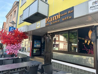 Außenansicht eines asiatischen Restaurants mit Sitzgelegenheiten im Freien und pinkem Kunstbaum.