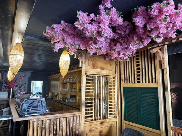 Ein japanisches Restaurant mit rosa Kirschblüten an der Decke über einem Holztresen im Inneren.