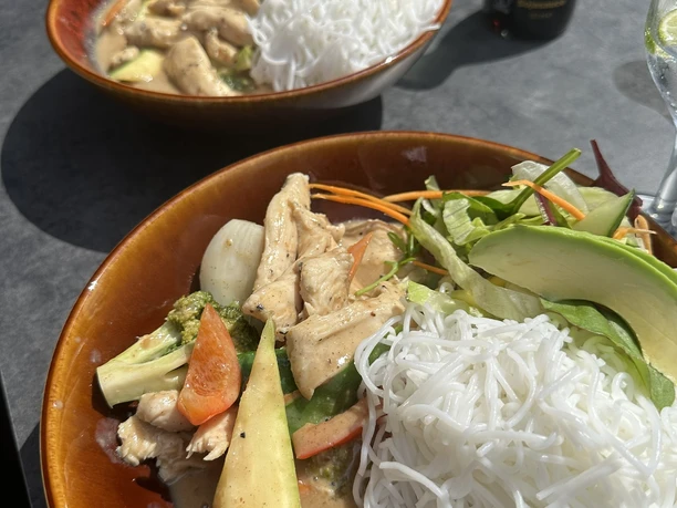 Zwei Schalen mit asiatischem Reisnudelsalat, frischem Gemüse und Hühnchen; im Hintergrund Sojasauce.