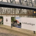 Schiffsanleger Benkhausen Werbeschild am Wasser unter einer Stahlbrücke; Hinweis auf Schloss, Café und Schiffsanleger.