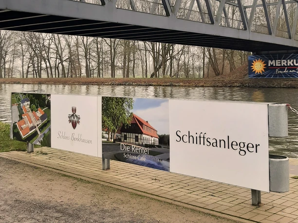 Schiffsanleger Benkhausen Werbeschild am Wasser unter einer Stahlbrücke; Hinweis auf Schloss, Café und Schiffsanleger.