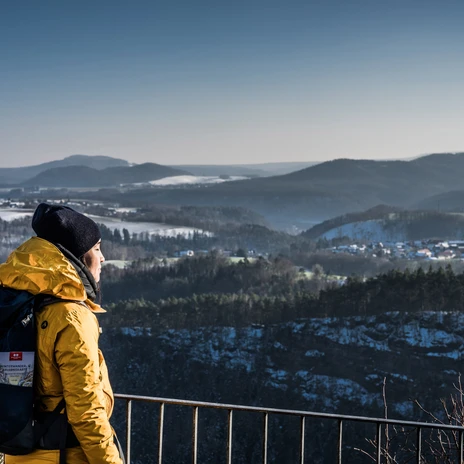 Brandaussicht Person in gelber Jacke betrachtet von Aussichtspunkt verschneite Landschaft und Wald im Winter.