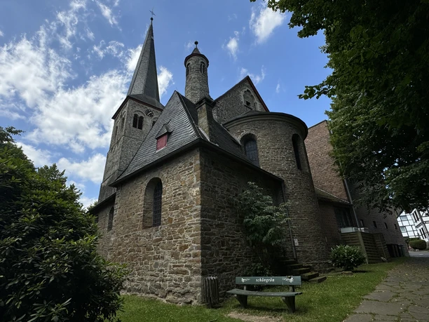 Kirche St. Walburga Historische Steinkirche mit Turm und Rundapsis, umgeben von Bäumen unter blauem Himmel.