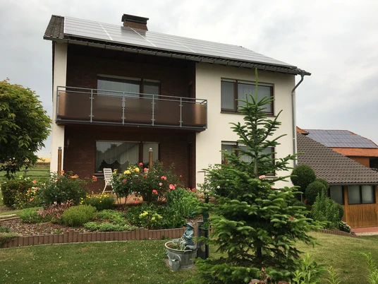 Fewo Güthoff aussen.jpg Zweistöckiges Haus mit Solarpaneelen, rotem Ziegel und Balkon, umgeben von gepflegtem Garten.