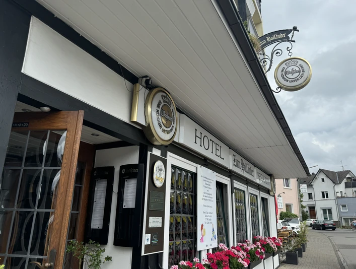 Hotel-Restaurant Zum Holländer - Außenansicht Hotelgebäude im Fachwerkstil mit Blumen und traditionellen Schildern. Hintergrund zeigt eine Straße.