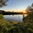 Angeln_in_der_Gemeinde_Rhauderfehn_IMG_3710.JPG Angeln am Flussufer bei Sonnenuntergang mit zwei Angelruten im Gras und ruhigem Wasser