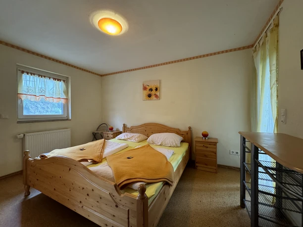 Gasthof Zum Stausee Gemütliches Schlafzimmer mit einem großen, hölzernen Doppelbett, gelber Bettwäsche und Sonnenblumen-Wandbild.