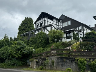Gasthof Zum Stausee Fachwerkhaus mit üppiger Begrünung an einem Hang, umgeben von Bäumen und bepflanzten Steingärten.