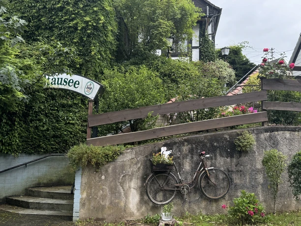 Gasthof Zum Stausee Fahrrad lehnt an einer Steinmauer, umgeben von üppigem Grün und Blumendekoration, nah an einem Fachwerkhaus.