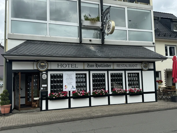 Hotel-Restaurant Zum Holländer - Außenansicht <p>Fachwerkfassade von "Hotel Zum Holländer" mit roten Blumen und schwarzem Schindeldach.</p>