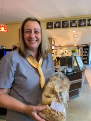 Eine lächelnde Frau in einem Café hält eine Tüte Gebäck in der Hand.