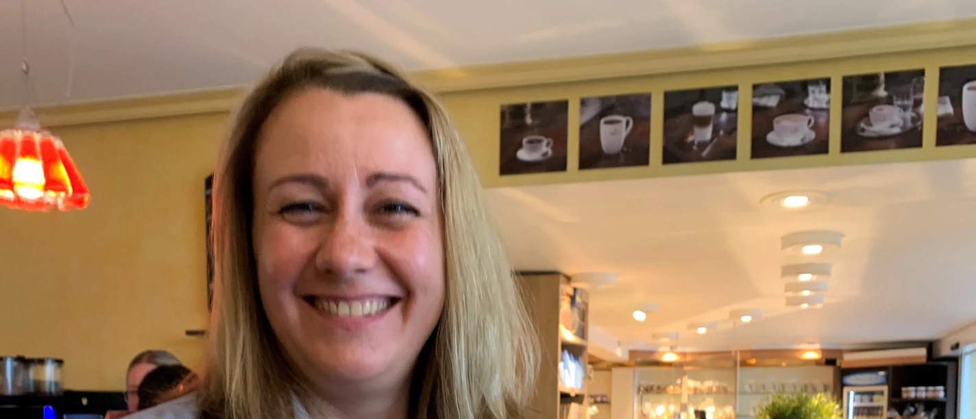 Eine lächelnde Frau in einem Café hält eine Tüte Gebäck in der Hand.