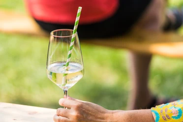 Weinmarkt Steinhagen (C) Dennis Neuschaefer-Rube.jpg Ein Glas Weißwein mit grün-weiß gestreiftem Strohhalm in der Sonne, gehalten von einer Hand.