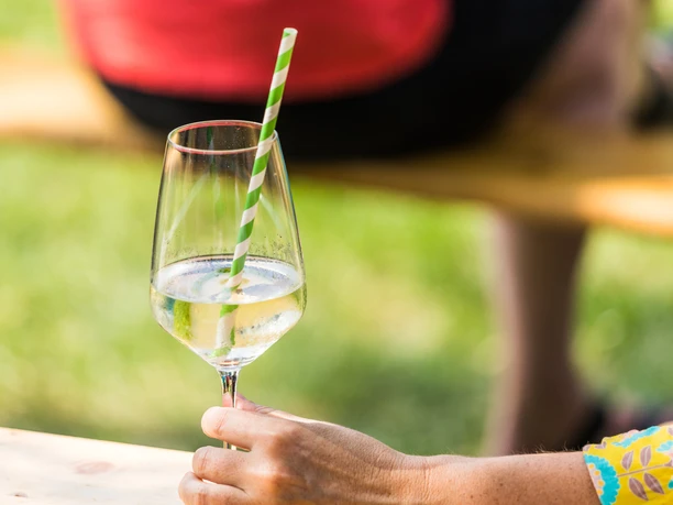 Weinmarkt Steinhagen (C) Dennis Neuschaefer-Rube.jpg Ein Glas Weißwein mit grün-weiß gestreiftem Strohhalm in der Sonne, gehalten von einer Hand.