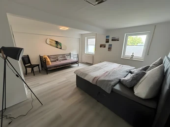 Schlafzimmer Fina Bornrows Helles Schlafzimmer mit einem großen Bett, einem Tagesbett und einer Stehlampe, minimalistisch dekoriert.