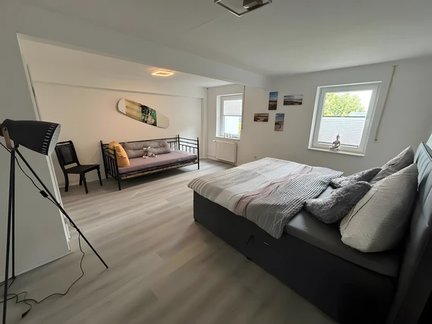 Schlafzimmer Fina Bornrows Helles Schlafzimmer mit einem großen Bett, einem Tagesbett und einer Stehlampe, minimalistisch dekoriert.