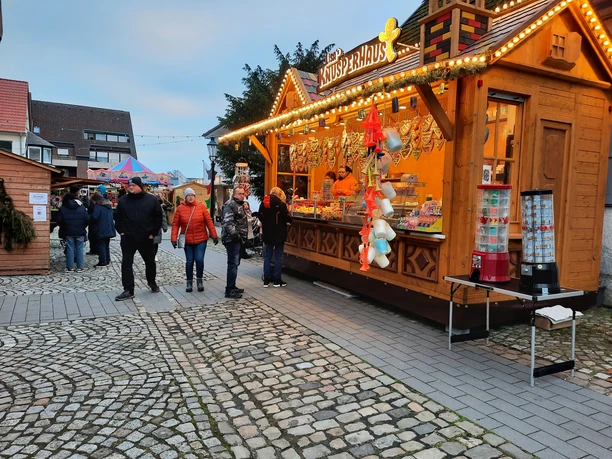 Weihnachtsmarkt Pr. Oldendorf Besucher flanieren über einen gepflasterten Weihnachtsmarkt mit beleuchteten Holzhütten und Dekoration.