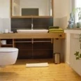 Franzbaeckerbad-200x150.jpeg Modernes Badezimmer mit Holzfußboden, Wandwaschbecken, wandhängender Toilette und grünen Handtüchern.