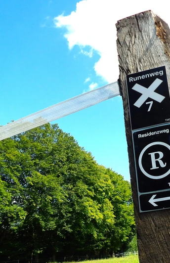 Holzpfosten trägt Schilder für Wanderwege im Teutoburger Wald, blauer Himmel, grüne Bäume im Hintergrund.