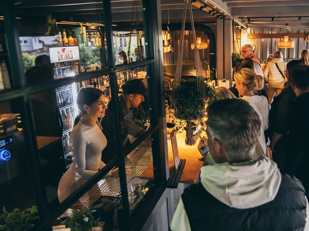 Strandlicht Freitag Eroeffnung-29.jpg Menschen genießen eine gesellige Eröffnungsfeier in einer stilvollen Bar mit warmem Licht und Getränken.